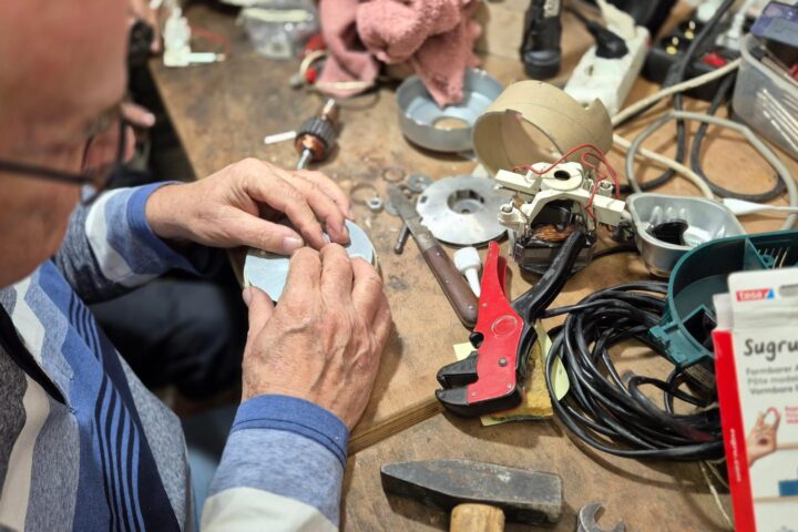 Ein Mann repariert an einem Arbeitstisch ein elektronisches Gerät mit Werkzeugen und Kabeln.