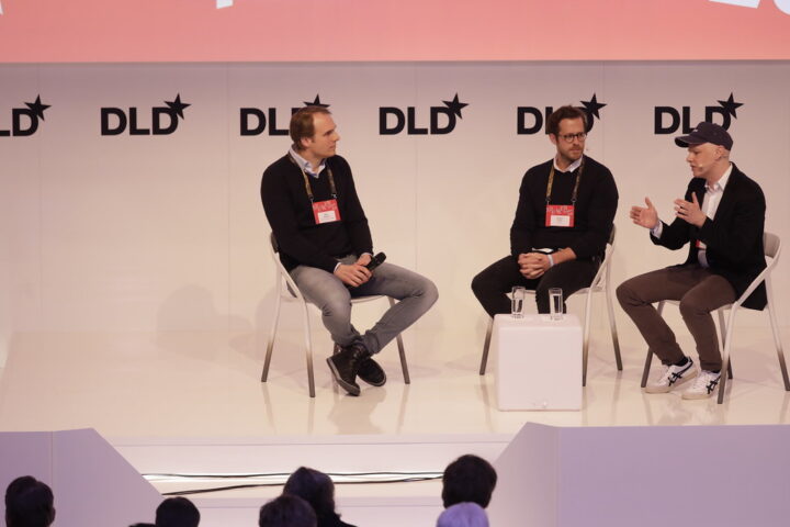Drei Männer sitzen auf einer DLD-Bühne bei einer Diskussion vor Publikum.