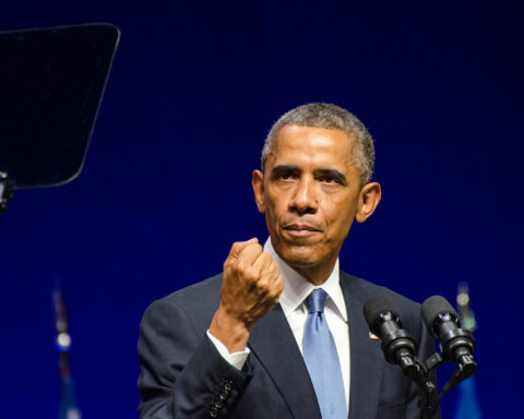 Barack Obama spricht an einem Podium mit Mikrofonen vor blauem Hintergrund.