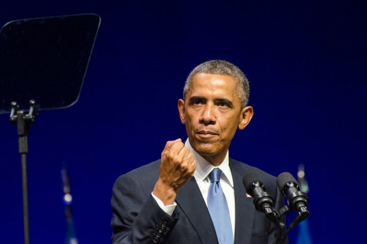 Barack Obama spricht an einem Podium mit Mikrofonen vor blauem Hintergrund.