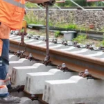 Arbeiter in orangefarbener Schutzkleidung bei Gleisbauarbeiten an einem Bahnstreckenabschnitt.