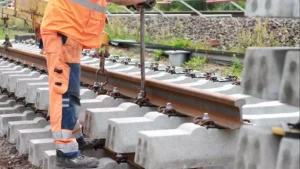 Arbeiter in orangefarbener Schutzkleidung bei Gleisbauarbeiten an einem Bahnstreckenabschnitt.