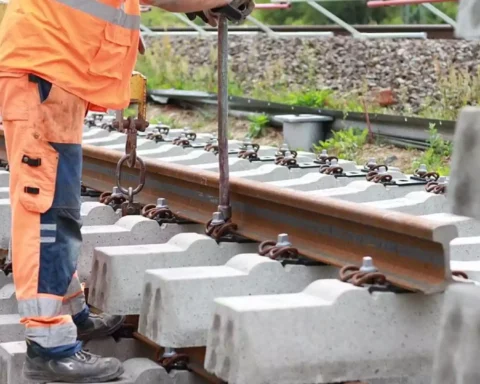 Arbeiter in orangefarbener Schutzkleidung bei Gleisbauarbeiten an einem Bahnstreckenabschnitt.