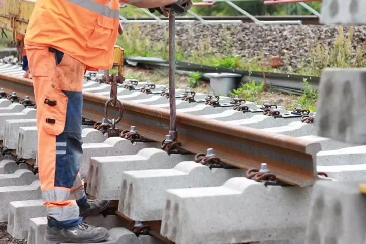 Arbeiter in orangefarbener Schutzkleidung bei Gleisbauarbeiten an einem Bahnstreckenabschnitt.
