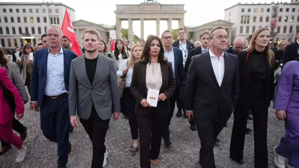 Mehrere Menschen gehen vor dem Brandenburger Tor in Berlin über den Platz.