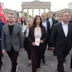 Mehrere Menschen gehen vor dem Brandenburger Tor in Berlin über den Platz.