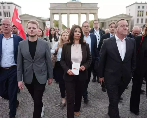 Mehrere Menschen gehen vor dem Brandenburger Tor in Berlin über den Platz.