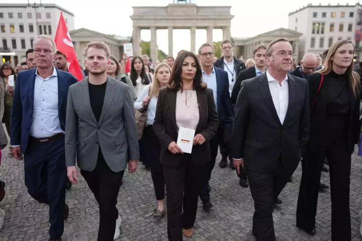 Mehrere Menschen gehen vor dem Brandenburger Tor in Berlin über den Platz.