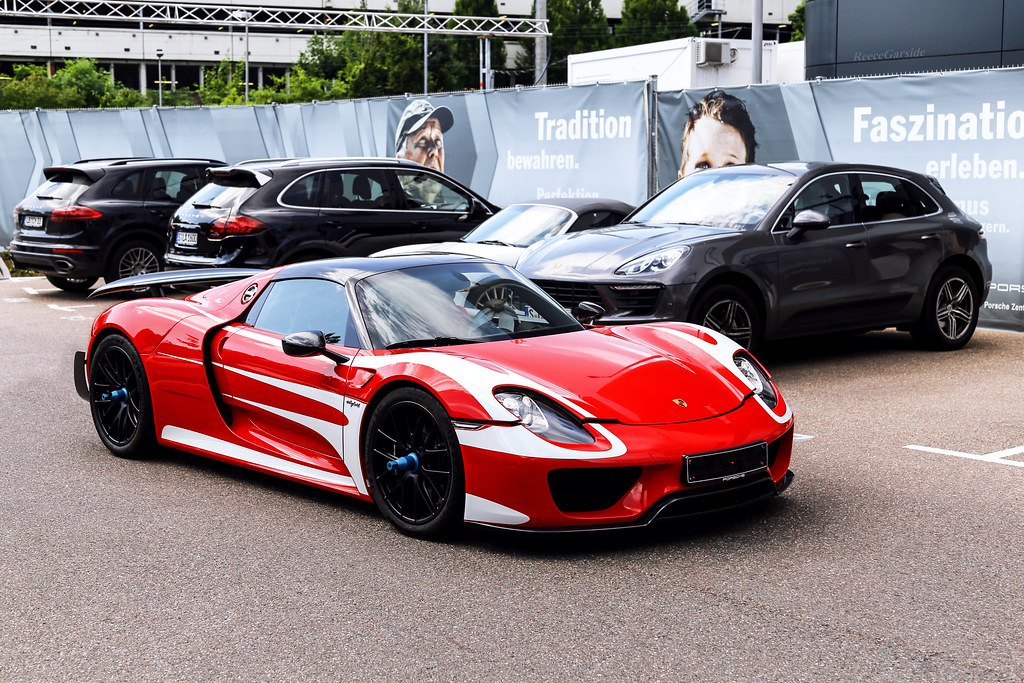 Roter Porsche-Supersportwagen steht vor mehreren schwarzen Porsche-SUVs auf einem Parkplatz.