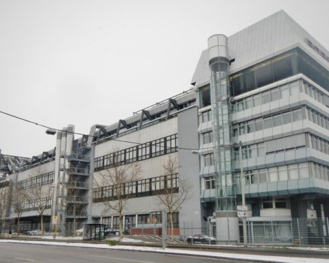 Außenansicht eines modernen Porsche-Gebäudes an einer Straße bei bewölktem Himmel.