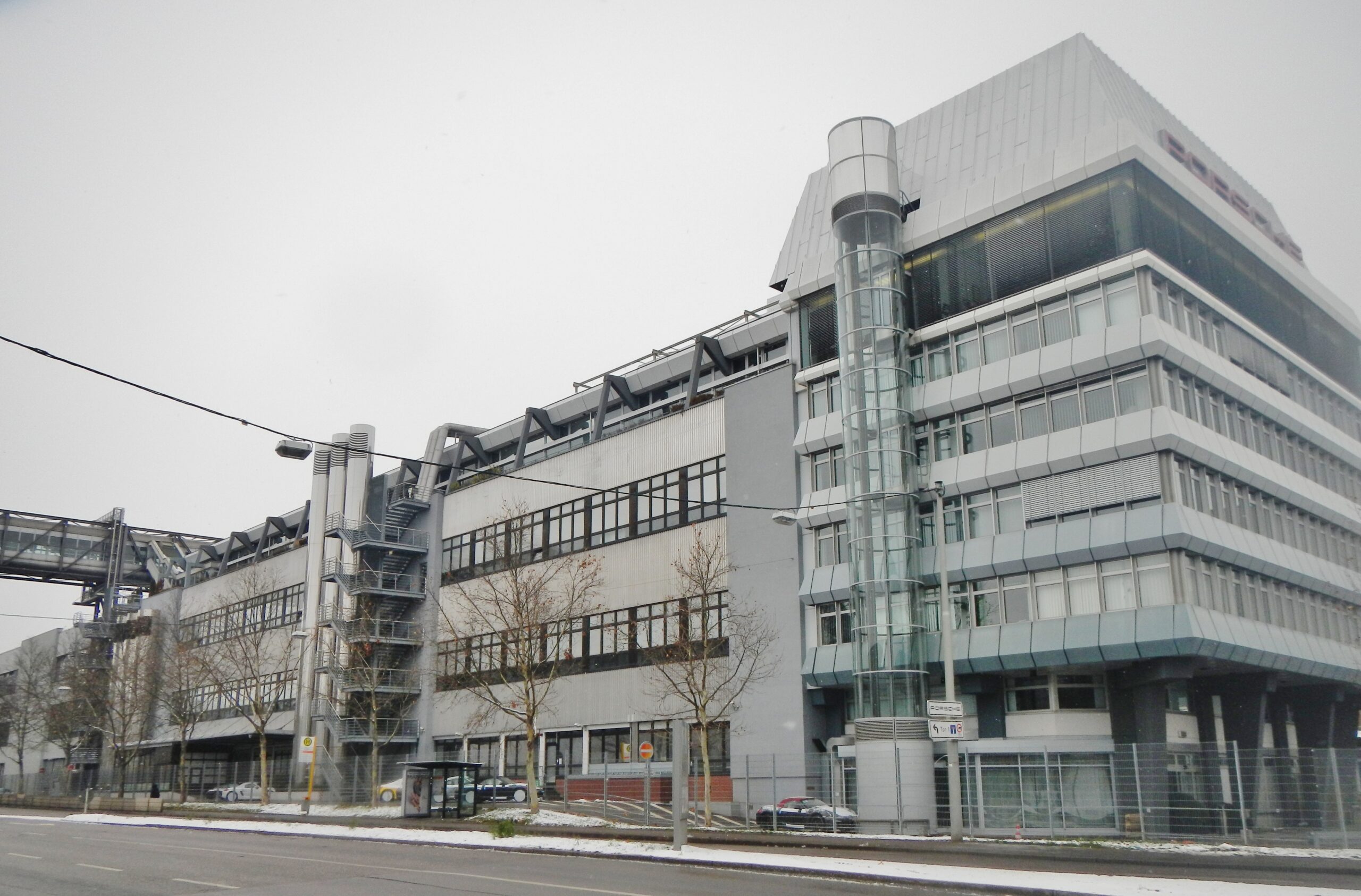 Außenansicht eines modernen Porsche-Gebäudes an einer Straße bei bewölktem Himmel.