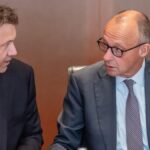 Zwei Männer im Anzug sprechen in einem Besprechungsraum miteinander.