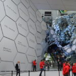 Besucher vor einem Audi-Exponat mit hexagonalem Wanddesign und Spiegelkonstruktion auf einer Automesse.