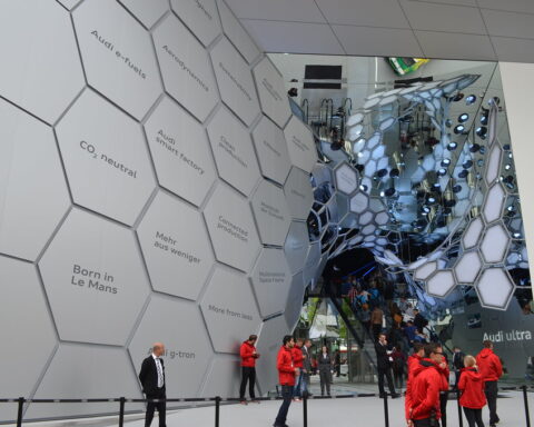 Besucher vor einem Audi-Exponat mit hexagonalem Wanddesign und Spiegelkonstruktion auf einer Automesse.