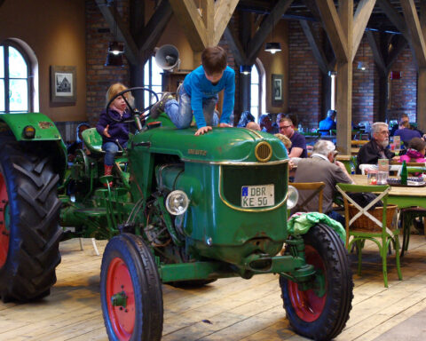 Grüner Deutz-Traktor in einem Innenraum mit mehreren Sitzenden im Hintergrund.