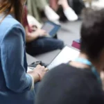 Mehrere sitzende Personen nutzen Laptops und Tablets bei einer Veranstaltung.