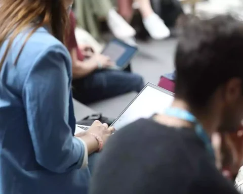 Mehrere sitzende Personen nutzen Laptops und Tablets bei einer Veranstaltung.