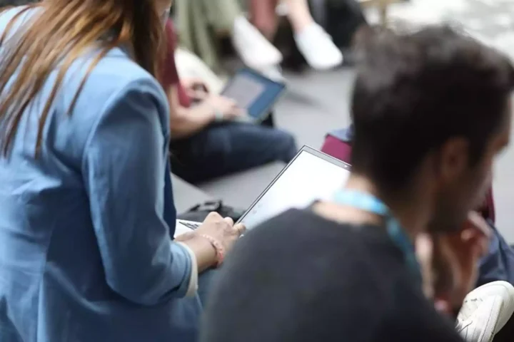 Mehrere sitzende Personen nutzen Laptops und Tablets bei einer Veranstaltung.