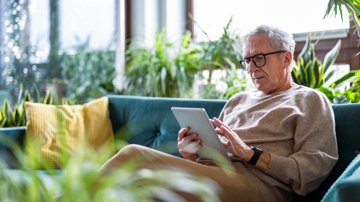 Älterer Mann sitzt auf einem Sofa und nutzt ein Tablet.