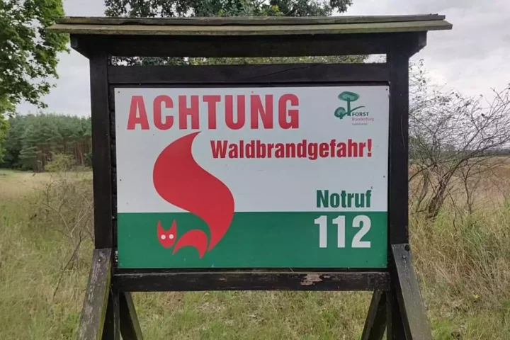 Warnschild mit der Aufschrift „Achtung Waldbrandgefahr“ und Notruf 112 an einem Waldrand.