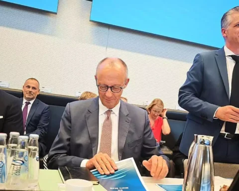Mehrere Politiker sitzen in einem Sitzungssaal an einem Tisch; ein Mann im Anzug spricht am Mikrofon.