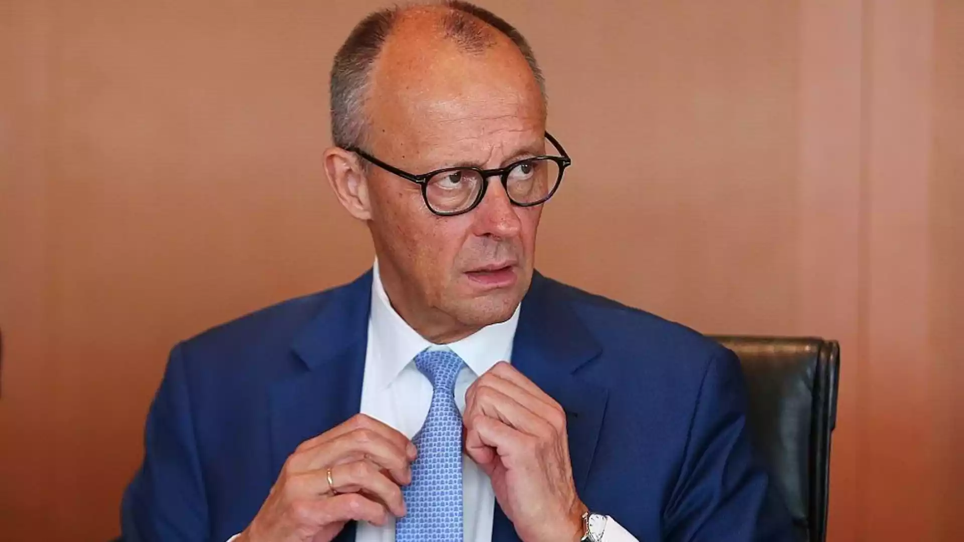 Mann im blauen Anzug und mit Brille richtet seine Krawatte.
