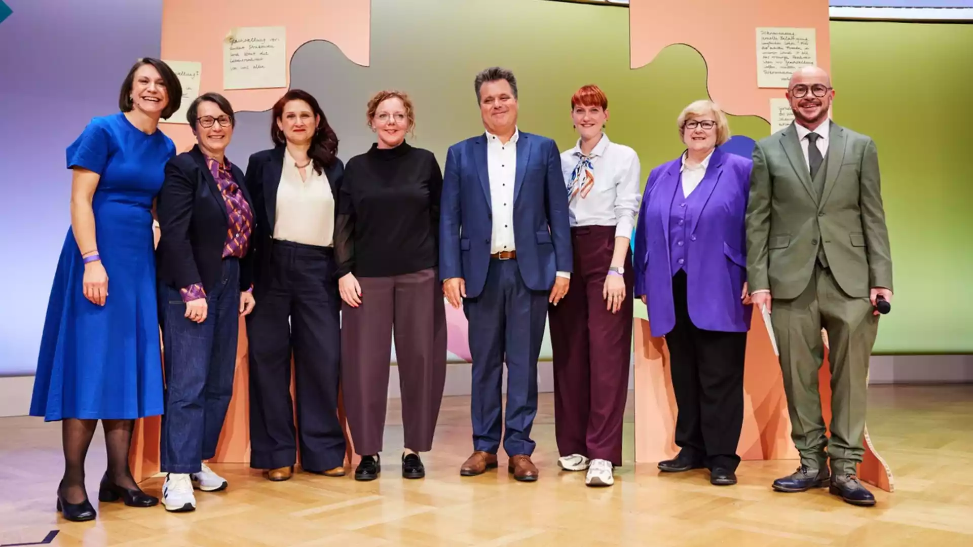 Bundesstiftung Gleichstellung veranstaltet dritten Gleichstellungstag in Berlin 1 Sieben Personen stehen auf einer Bühne vor einer bunten Wanddekoration.