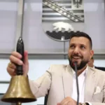 Mann in hellem Anzug läutet in einem Parlamentssaal eine Glocke am Rednerpult.