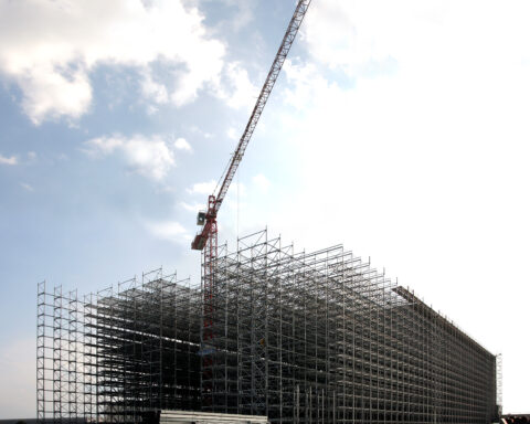 Große Baustelle mit Stahlgerüst und Baukran vor bewölktem Himmel.