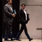 Drei Männer in Anzügen verlassen ein Gebäude am Abend.