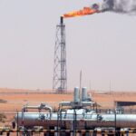Gasfackel auf einer Industrieanlage in der Wüste mit Rohrleitungen im Vordergrund.
