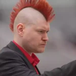 Sascha Lobo mit rotem Irokesenschnitt schaut auf ein Smartphone.