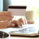Hand hält eine Bankkarte vor einem Laptop beim Online-Banking.