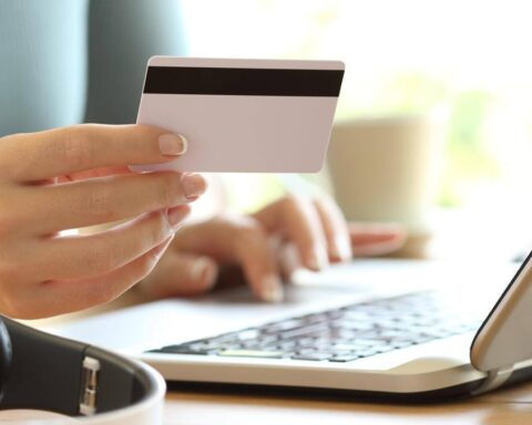 Hand hält eine Bankkarte vor einem Laptop beim Online-Banking.