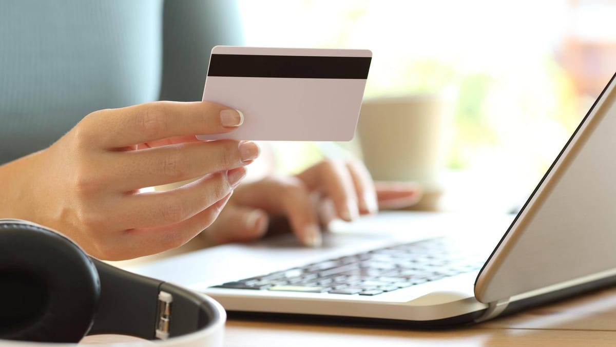 Banküberweisung zurückholen: Wann Banken Geld stoppen und was es kostet 1 Hand hält eine Bankkarte vor einem Laptop beim Online-Banking.
