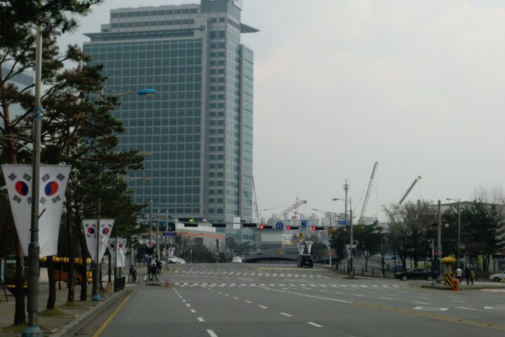 Straße in Seoul mit einem Samsung-Gebäude im Hintergrund und südkoreanischen Flaggen am Straßenrand.