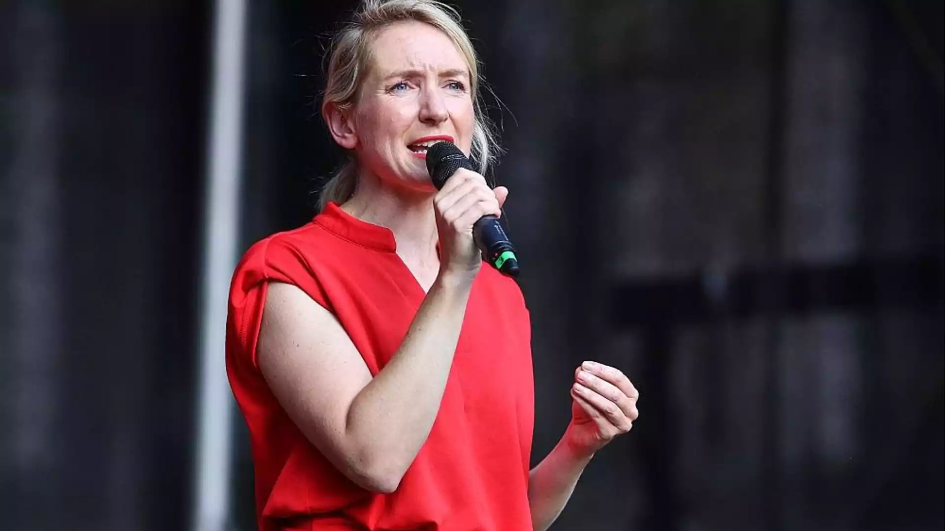 Ines Schwerdtner spricht mit einem Mikrofon auf einer Bühne und trägt ein rotes Oberteil.