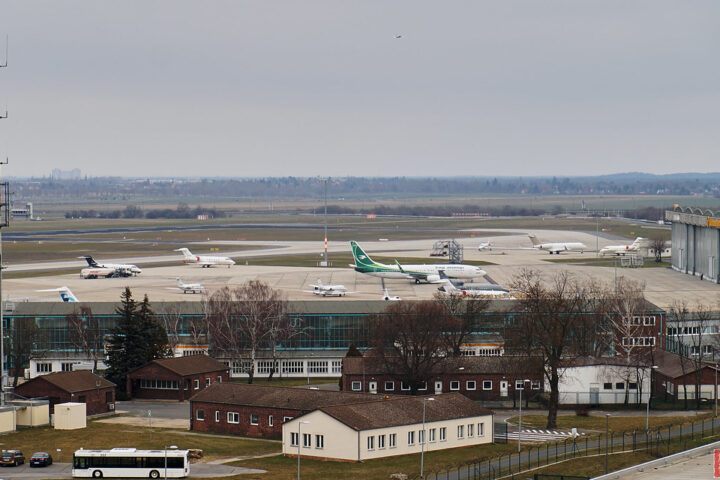 Mehrere Ryanair-Flugzeuge stehen auf dem Vorfeld eines Flughafens mit Start- und Landebahn im Hintergrund.