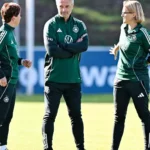 Christian Wück spricht mit zwei Trainerinnen auf einem Fußballtrainingsplatz.