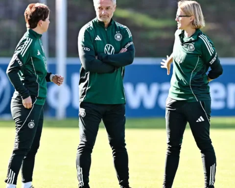 Christian Wück spricht mit zwei Trainerinnen auf einem Fußballtrainingsplatz.