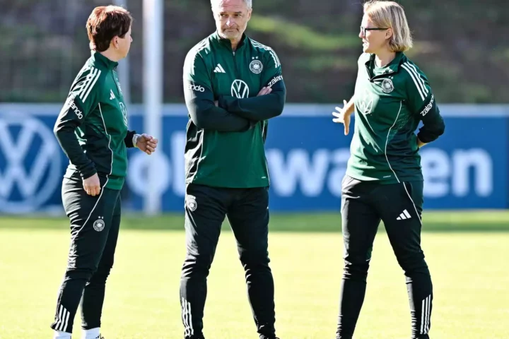 Christian Wück spricht mit zwei Trainerinnen auf einem Fußballtrainingsplatz.