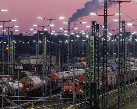 Güterzüge und Rangiergleise in einem beleuchteten Bahnbetriebswerk bei Abendhimmel.