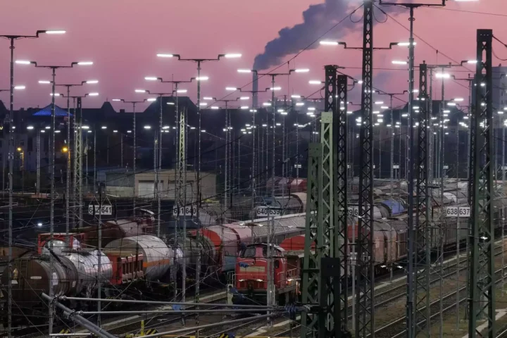 Güterzüge und Rangiergleise in einem beleuchteten Bahnbetriebswerk bei Abendhimmel.