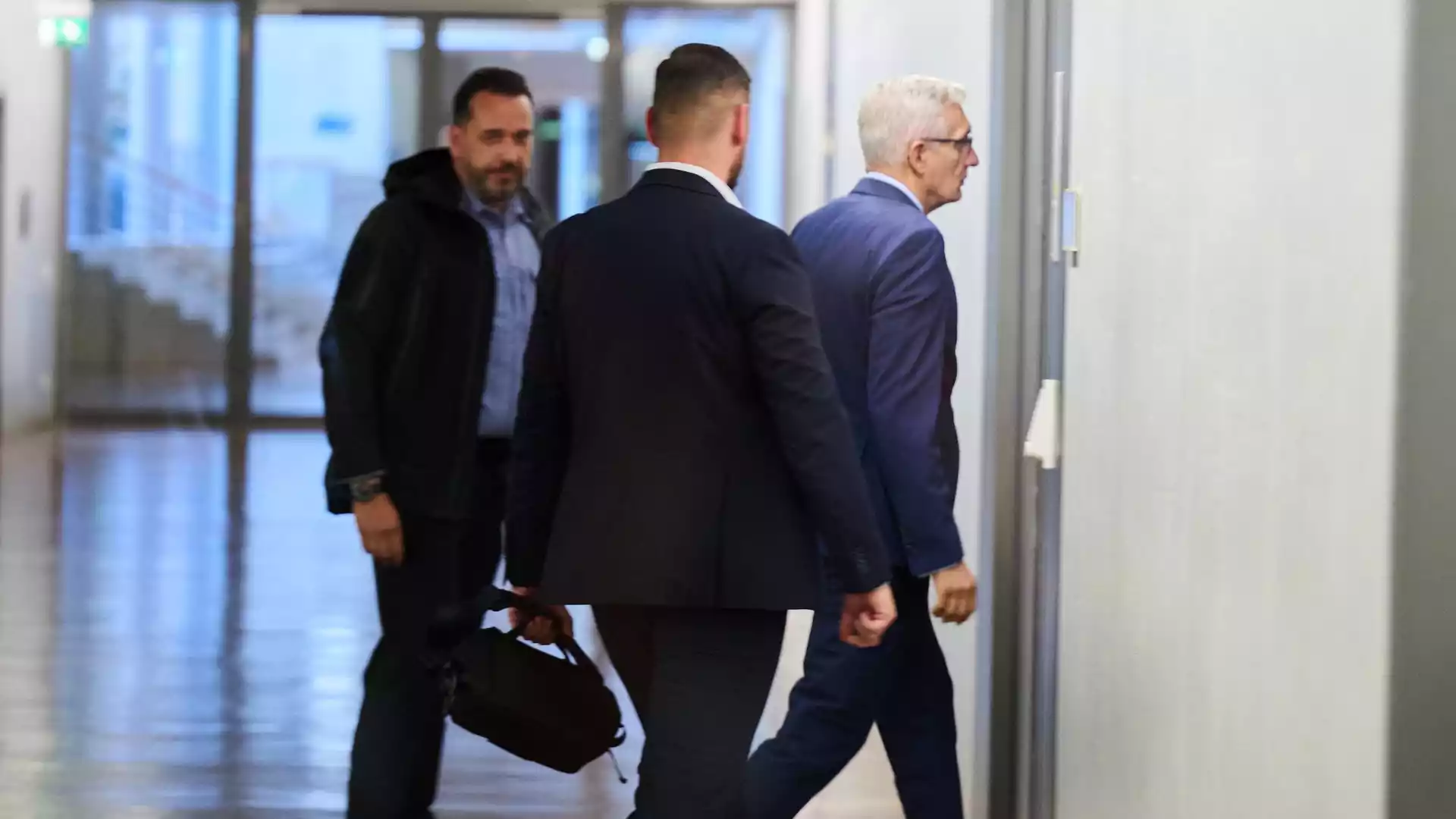 PKGr untersucht mutmaßlichen Spionagefall um Ex-BND-Chef Hanning 1 Drei Männer gehen durch einen hellen Flur, darunter ein älterer Mann im blauen Anzug mit weißen Haaren.