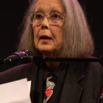 Anne Carson spricht an einem Mikrofon auf einer Bühne.