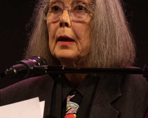 Anne Carson spricht an einem Mikrofon auf einer Bühne.