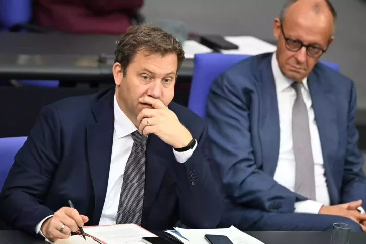 Zwei Politiker sitzen bei einer Besprechung an einem Tisch, einer macht sich Notizen und wirkt nachdenklich.