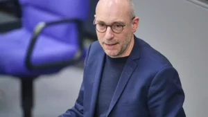 Mann mit Brille in blauem Sakko in einem Innenraum.