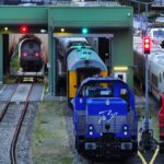 Mehrere Lokomotiven stehen in einem Bahndepot vor einer Waschanlage und auf Gleisen.