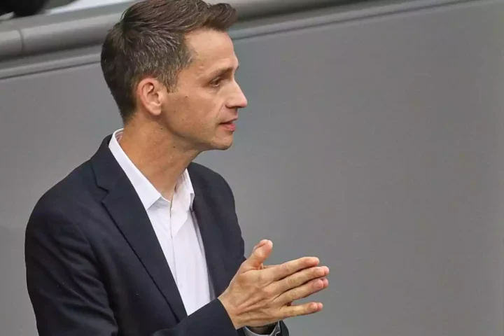 Andreas Audretsch im dunklen Anzug bei einer politischen Veranstaltung, im Profil und mit gefalteten Händen.